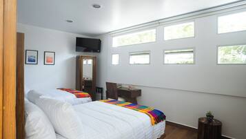 A bedroom with two beds, a TV, a desk, and multiple windows.
