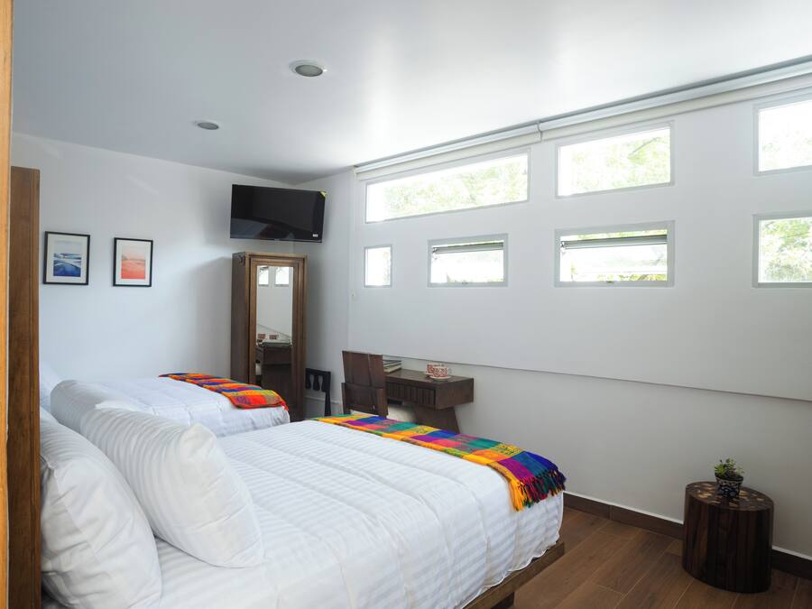 A bedroom with two beds, a TV, a desk, and multiple windows.