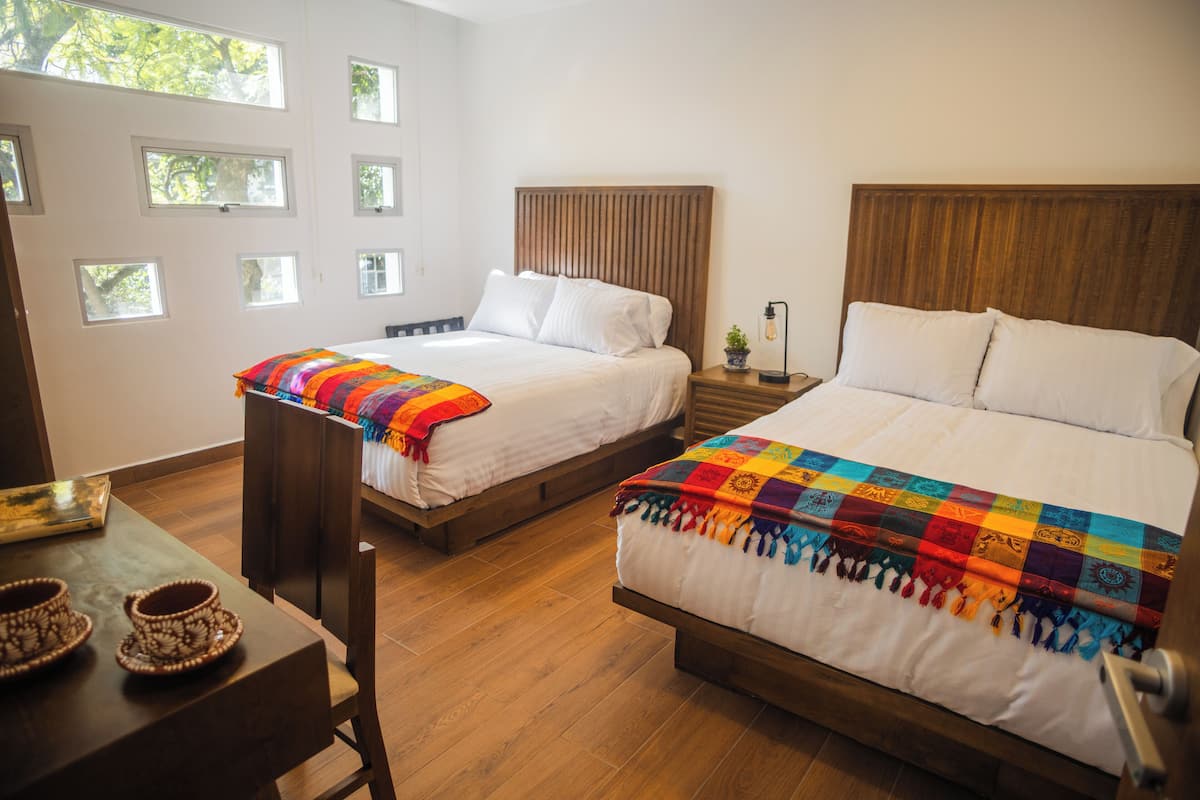 Habitación de hotel con dos camas, cabeceros de madera y una mesita con cuencos decorativos.