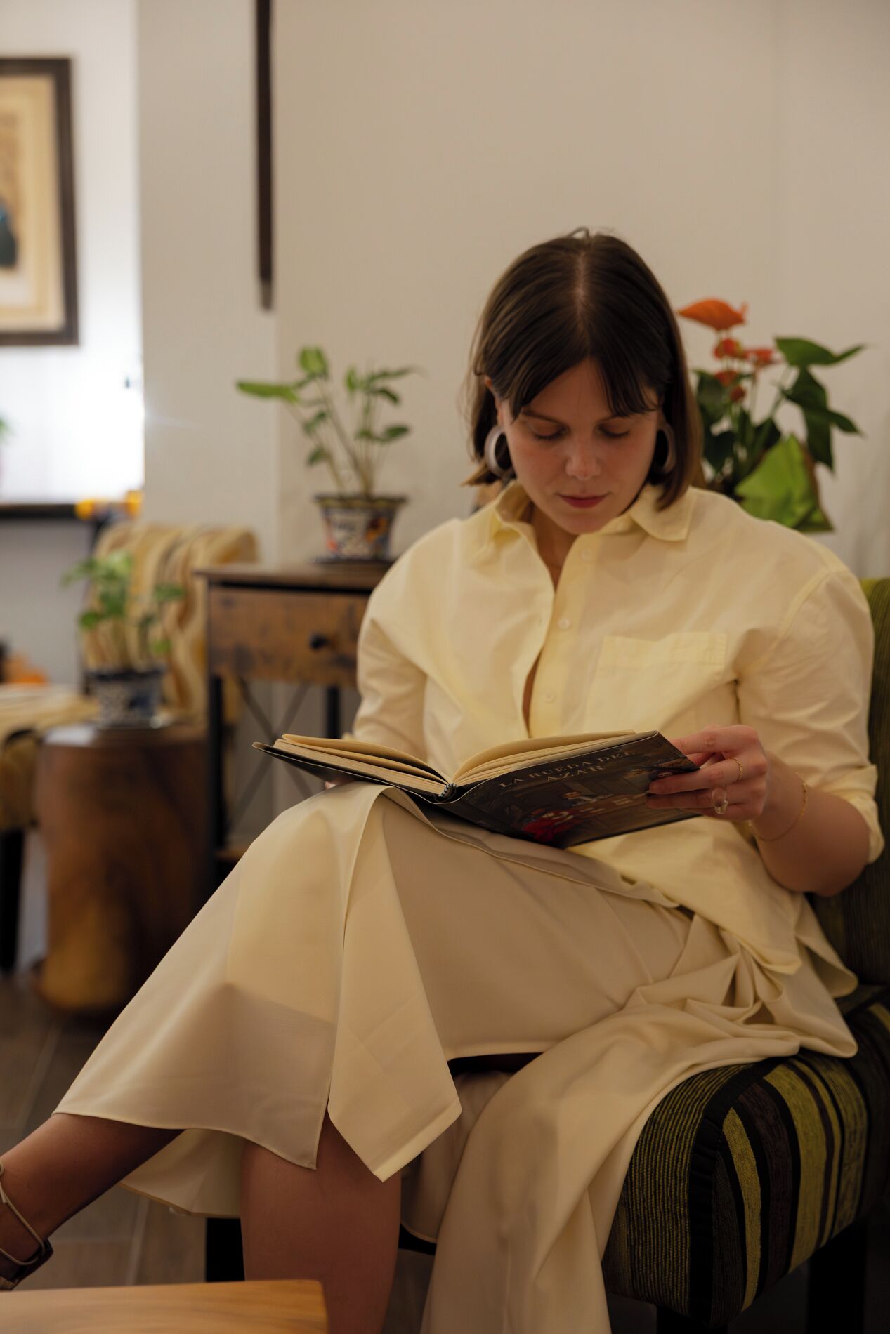 Una persona sentada en un sofá a rayas, leyendo un libro.