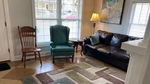 A living room with a patterned rug, a green armchair, a wooden chair, a black leather sofa, and a painting on the wall. - Cozy Apartment in the heart of town. Monthly min. (Bowling Green)
