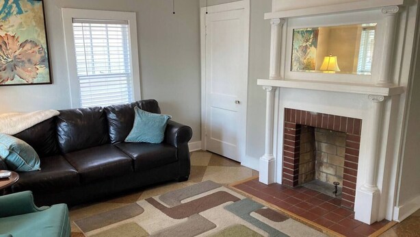 A living room with a fireplace, a black leather sofa, a teal armchair, and a patterned rug. - Cozy Apartment in the heart of town. Monthly min. (Bowling Green)