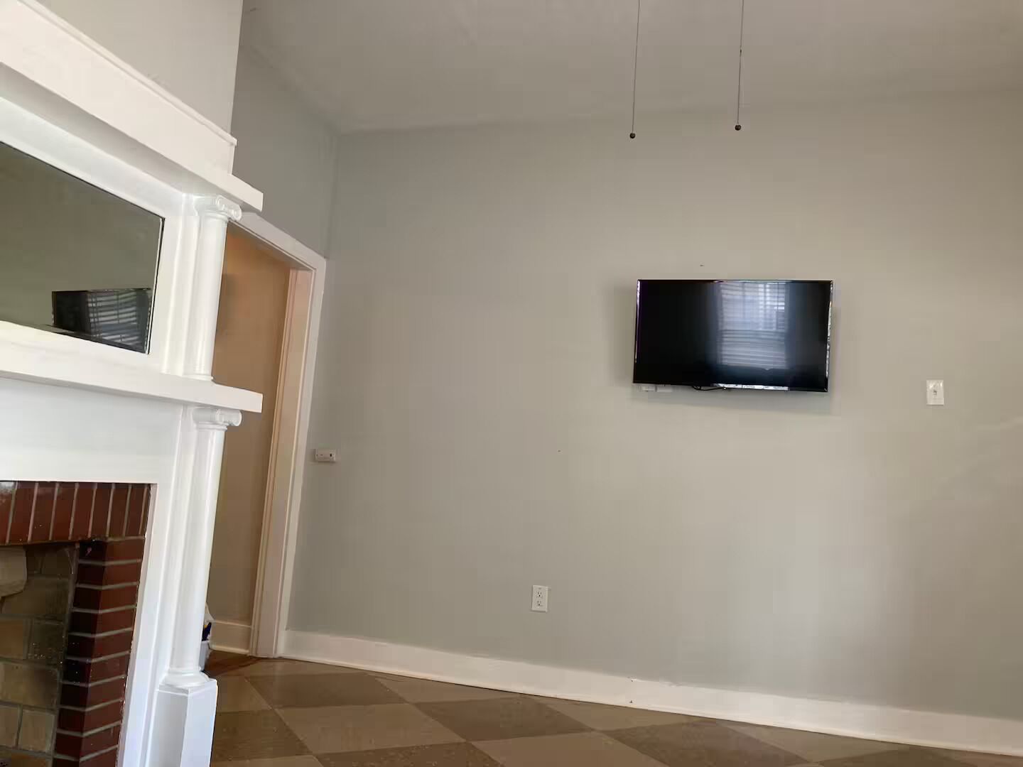 A room with a flat-screen TV mounted on the wall, a white mantelpiece, and a checkered floor.