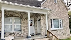 A stone house with a porch, a front door, and a staircase leading to the entrance. - Cozy Apartment in the heart of town. Monthly min. (Bowling Green)