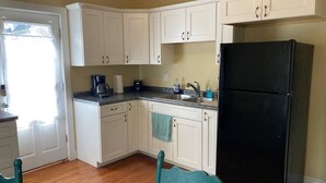 Una cocina con armarios blancos, un refrigerador negro, una cafetera y un lavamanos.