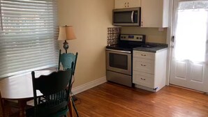 Cocina compacta con microondas, horno y armarios blancos. Hay una mesa de comedor con sillas y una lámpara.