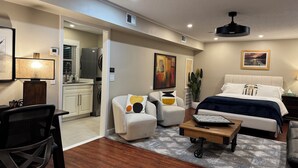 Una habitación de hotel moderna con cama, escritorio, silla y una kitchenette pequeña.