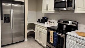Una cocina moderna con electrodomésticos de acero inoxidable, armarios blancos y una encimera con cafetera y frascos.