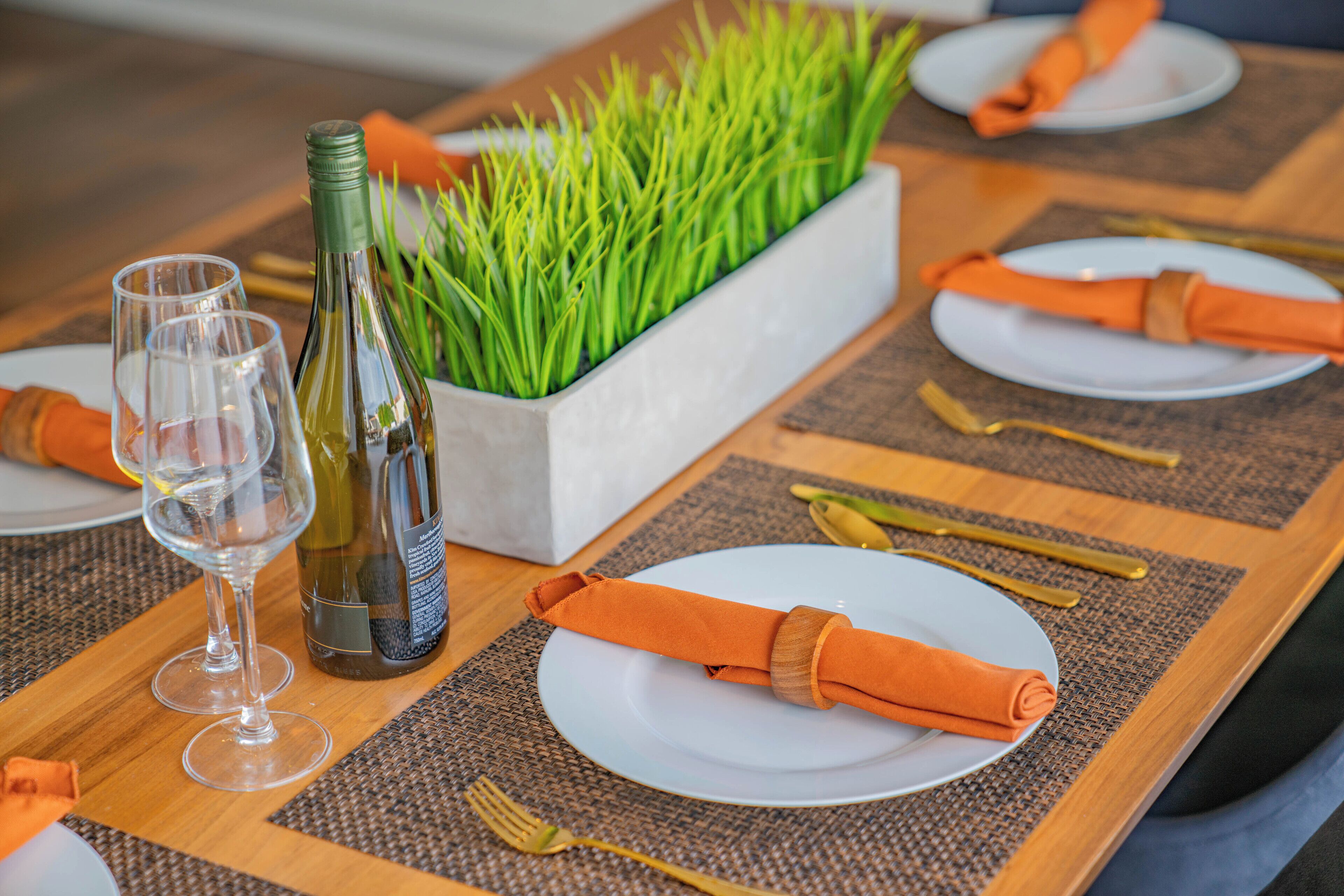 Una mesa de comedor dispuesta con platos, cubiertos y una botella de vino.