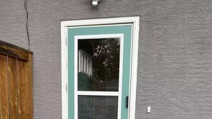 En turkis dør med et vindue, en trædørkarm, en dørmåtte med teksten "Oh, hello" og en potteplante med blomster.