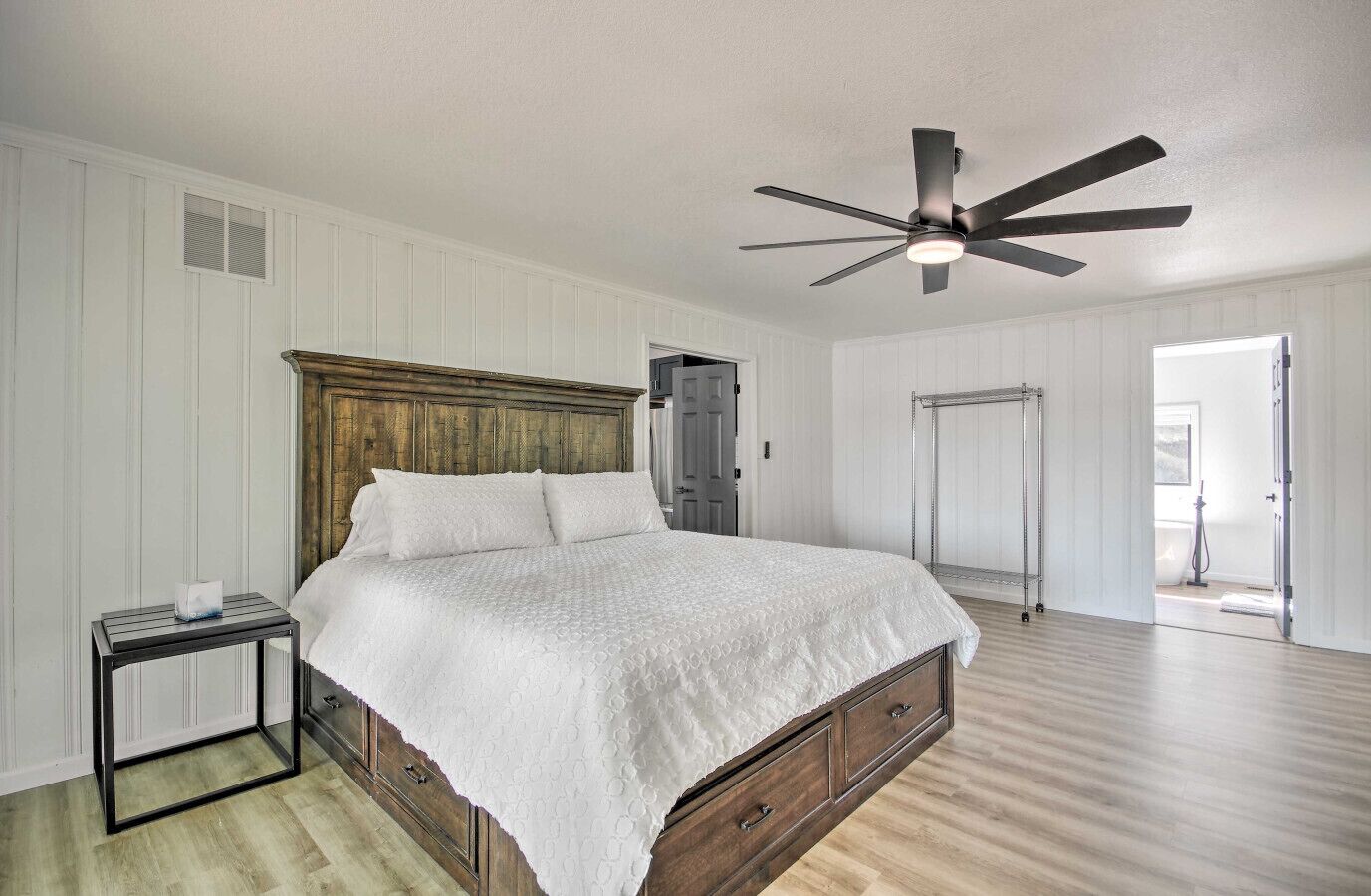 Quarto com cabeceira de madeira, cama com roupa de cama branca, mesa de cabeceira, ventilador de teto e closet espaçoso.