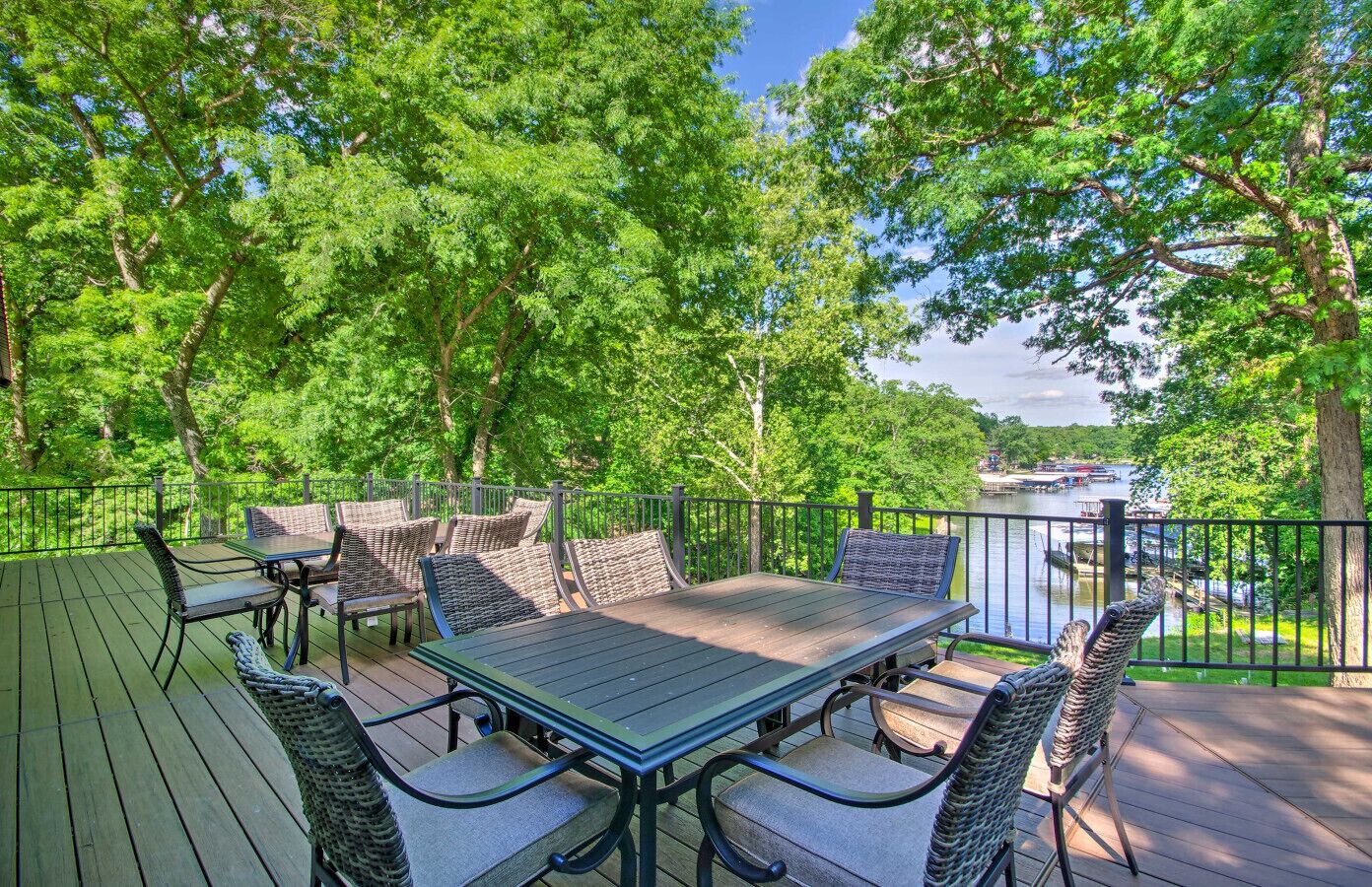 A wooden deck with a table and chairs, surrounded by trees and overlooking a body of water.