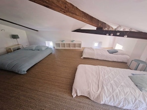 Une chambre avec trois lits, un plafond avec des poutres apparentes et une petite table avec une lampe.