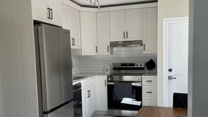 A modern kitchen with white cabinets, stainless steel appliances, and a wooden dining table.