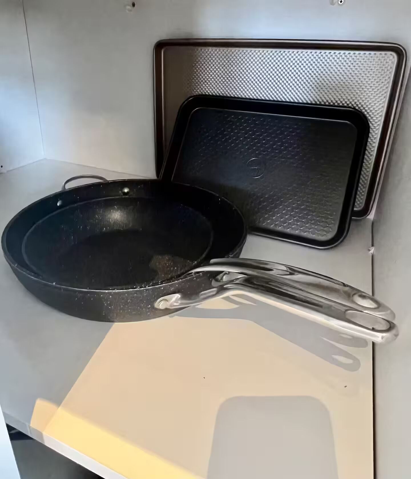 Una padella nera con lungo manico e una superficie antiaderente quadrata su un piano bianco.