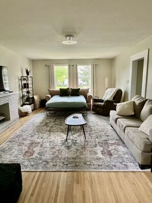 Een ruime woonkamer met een groot bed, twee sofa’s, een salontafel en een open haard.