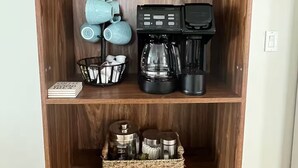 A wooden cabinet with a coffee maker, mugs, and storage containers.
