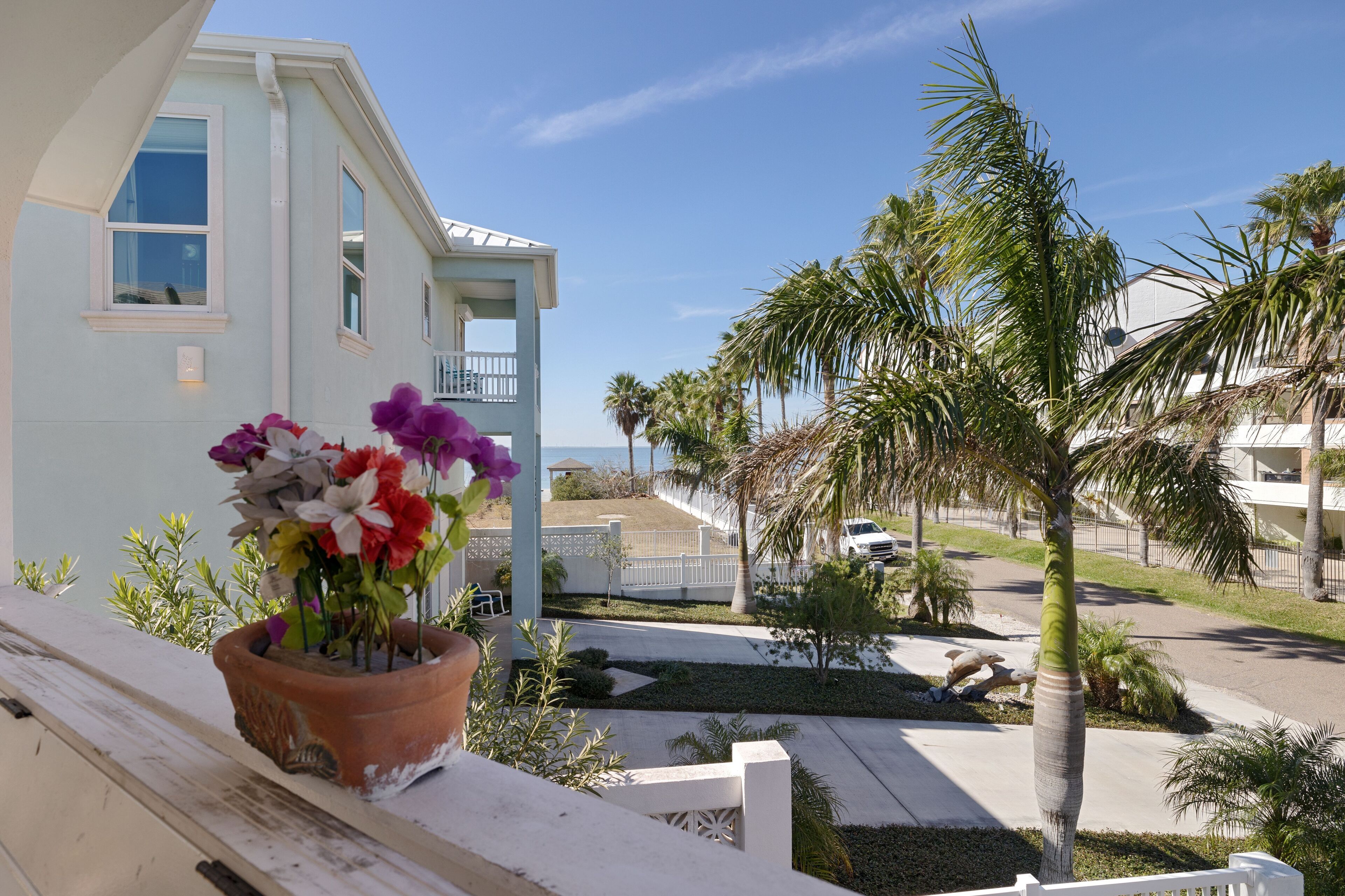 A residential building with a balcony, a flower pot with flowers, and a palm tree.