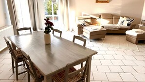 Un comedor con una mesa y sillas de madera, un florero con flores y vistas al exterior a través de una ventana con cortinas.