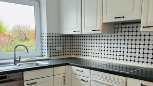 Una cocina con armarios blancos, encimera negra y salpicadero de azulejos.