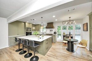 Una cocina amplia con una isla grande, taburetes de bar y un comedor con una mesa redonda y sillas.