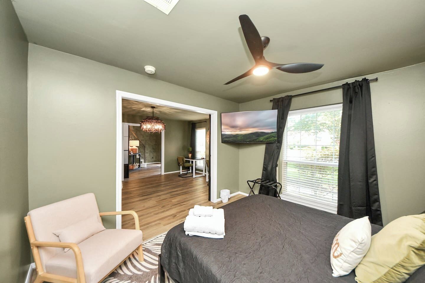 A bedroom with a bed, a chair, a TV, and a ceiling fan.