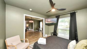 A bedroom with a bed, a chair, a TV, and a ceiling fan.