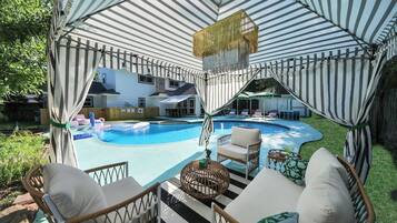 Un espacio exterior techado con piscina, sillas de descanso y una mesa de comedor.