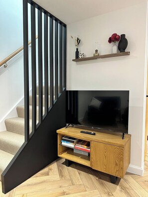 Una sala de estar moderna con una escalera, un televisor de pantalla plana, un mueble de entretenimiento de madera y una estantería con objetos decorativos.