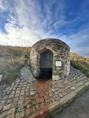 Una construcción de piedra con una puerta de metal, rodeada de hierba y un camino empedrado.