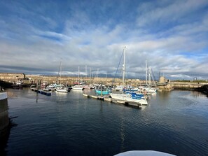 Un puerto deportivo con barcos amarrados a muelles, agua tranquila y una vista distante de una estructura fortificada.