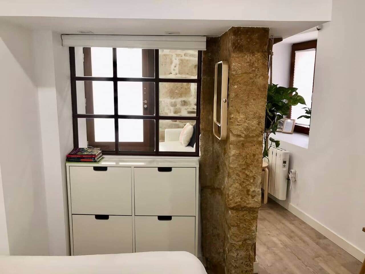 Una habitación pequeña con ventana, un armario blanco, un radiador y una planta.