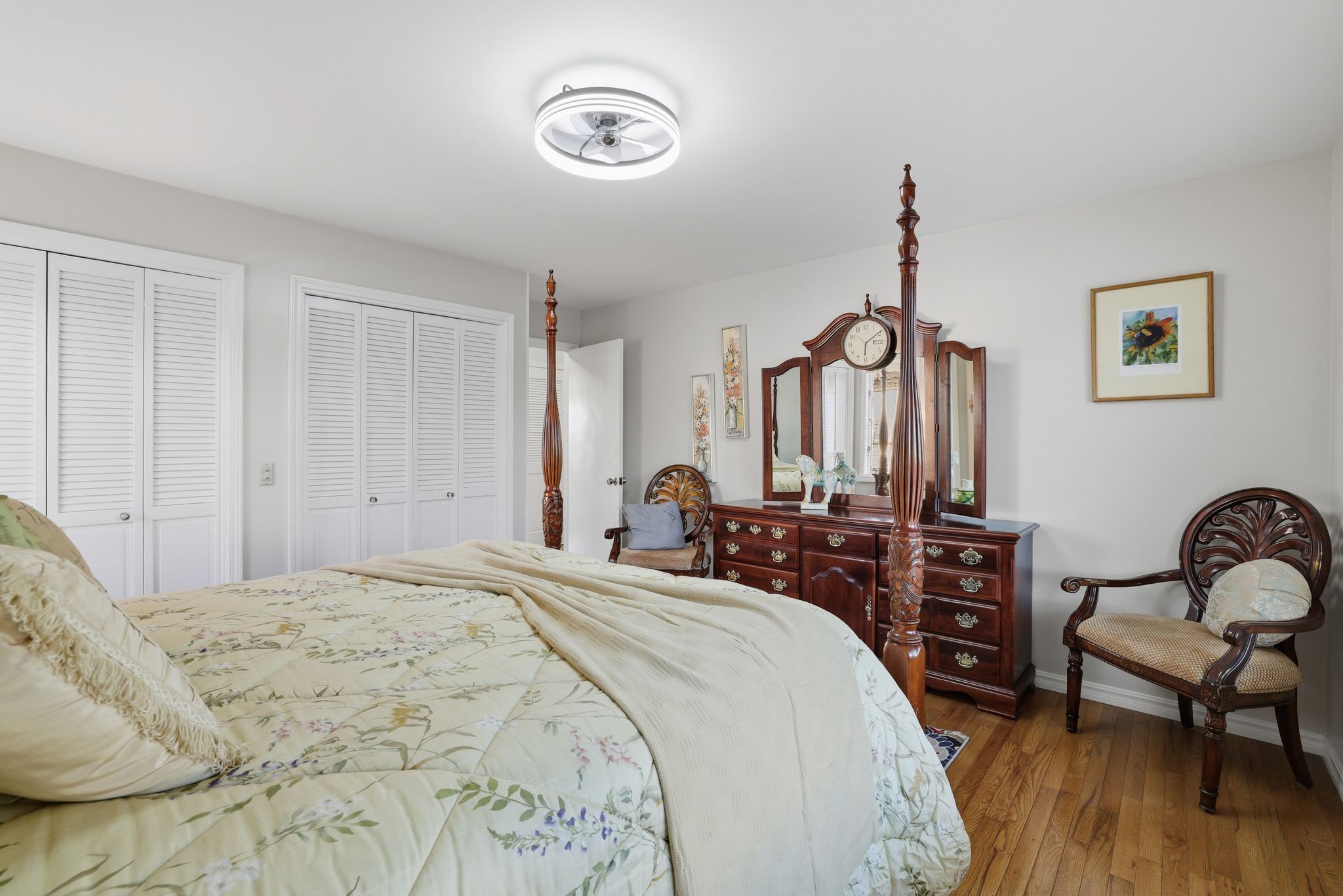 Une chambre à coucher avec un grand lit, une commode en bois, une chaise et un ventilateur de plafond.