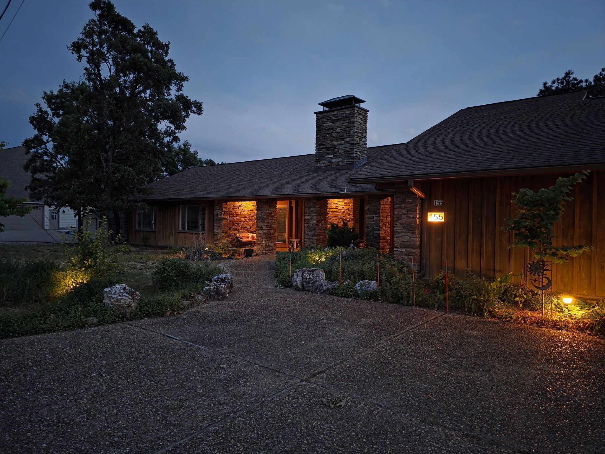 Une maison en pierre avec une cheminée, une allée et une entrée bien éclairée.