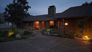 Een stenen huis met schoorsteen, oprit en een goed verlichte ingang.
