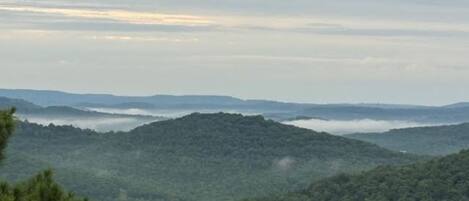 A panoramic view of a mountainous landscape with dense forests and a layer of clouds below.