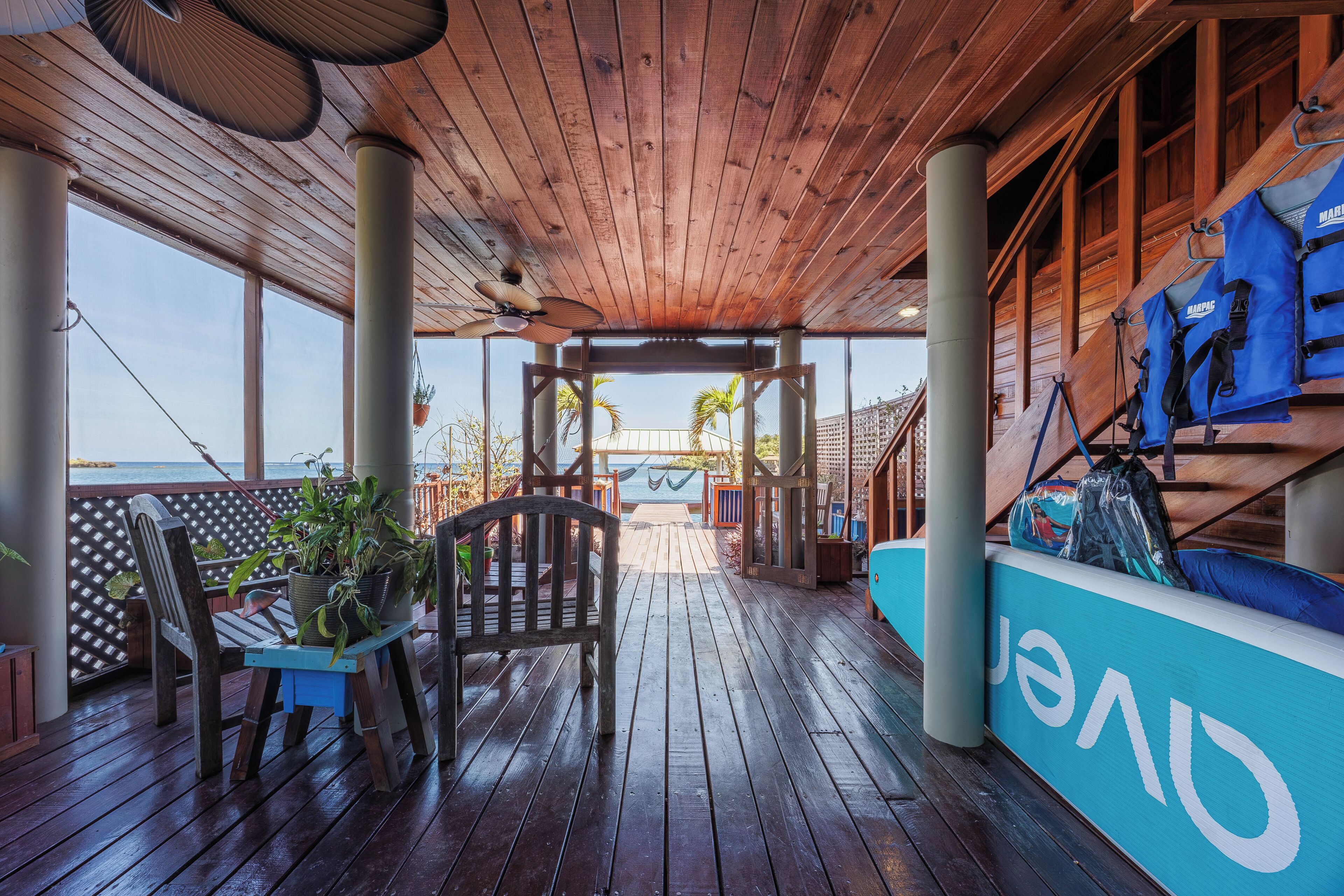 A wooden deck with a view of the ocean, a seating area with a table and chairs, and a blue lifeguard stand.