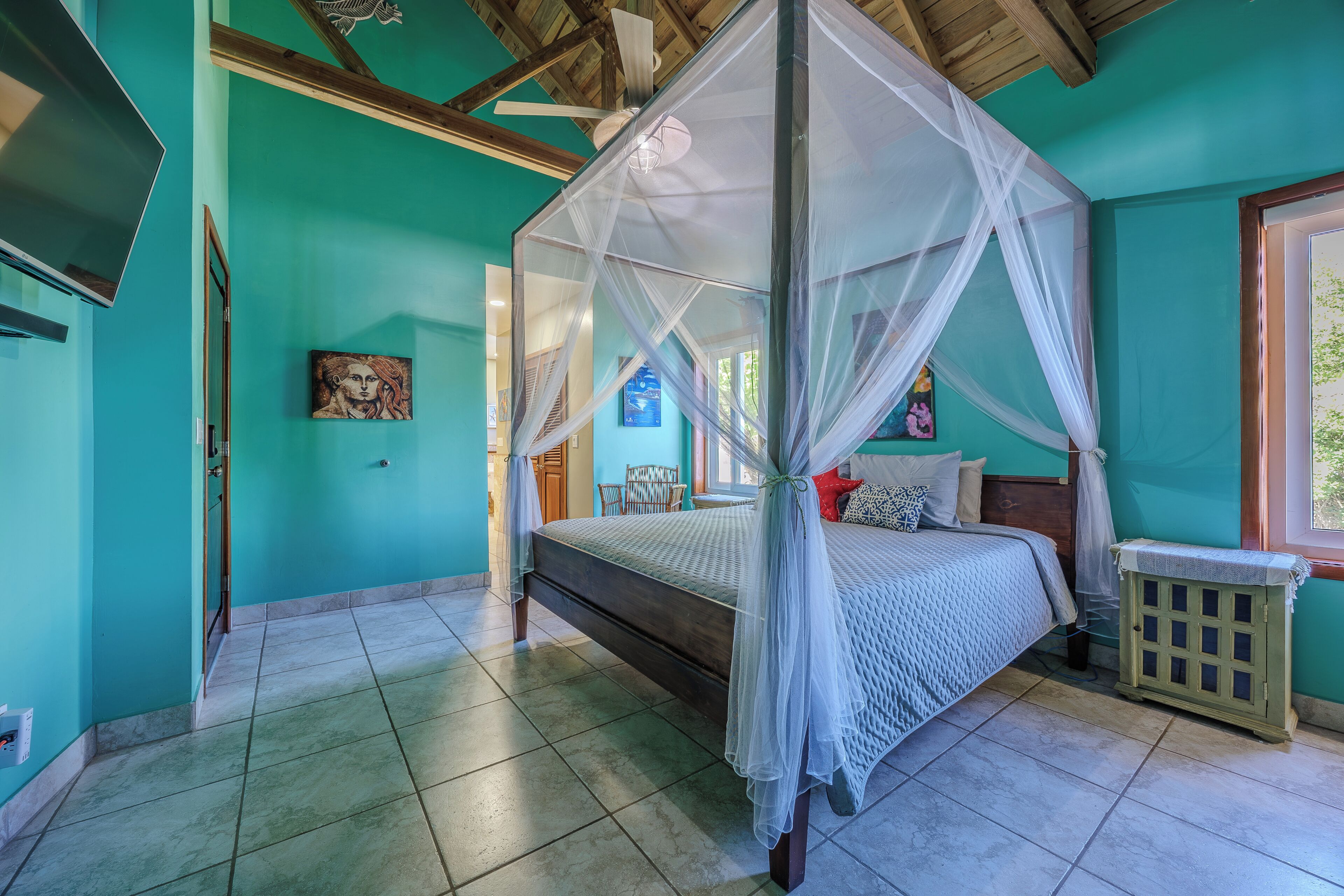 A bedroom with a bed, a TV, a mosquito net, and a small cabinet.