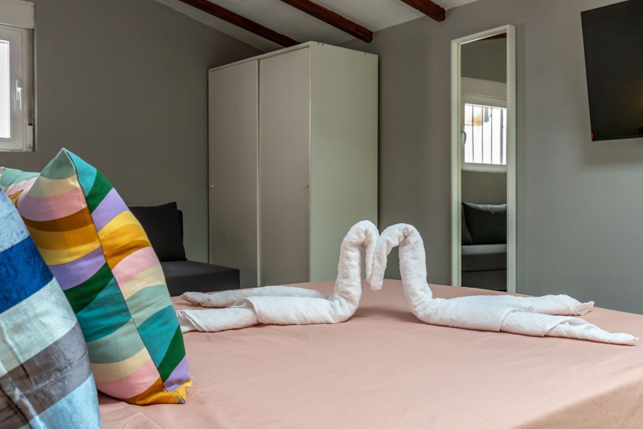 A hotel room with a bed, a colorful striped pillow, a white wardrobe, and a mirror.