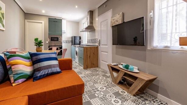 Ett kompakt bostadsutrymme med ett litet kök, en soffa med randiga kuddar och en tv som är monterad på väggen.