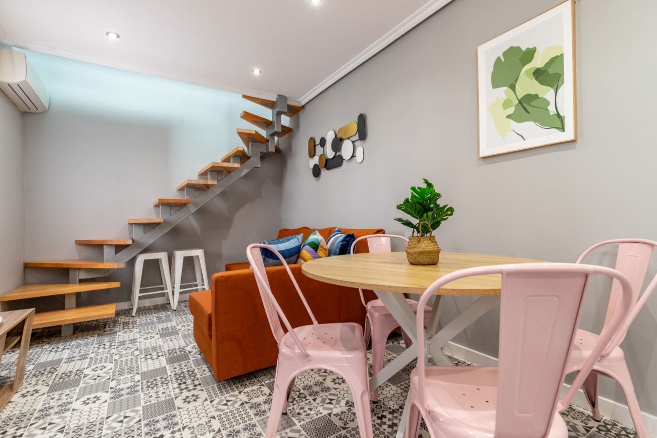 Ein modernes Interieur mit Treppe, einem runden Holztisch und rosa Stühlen.