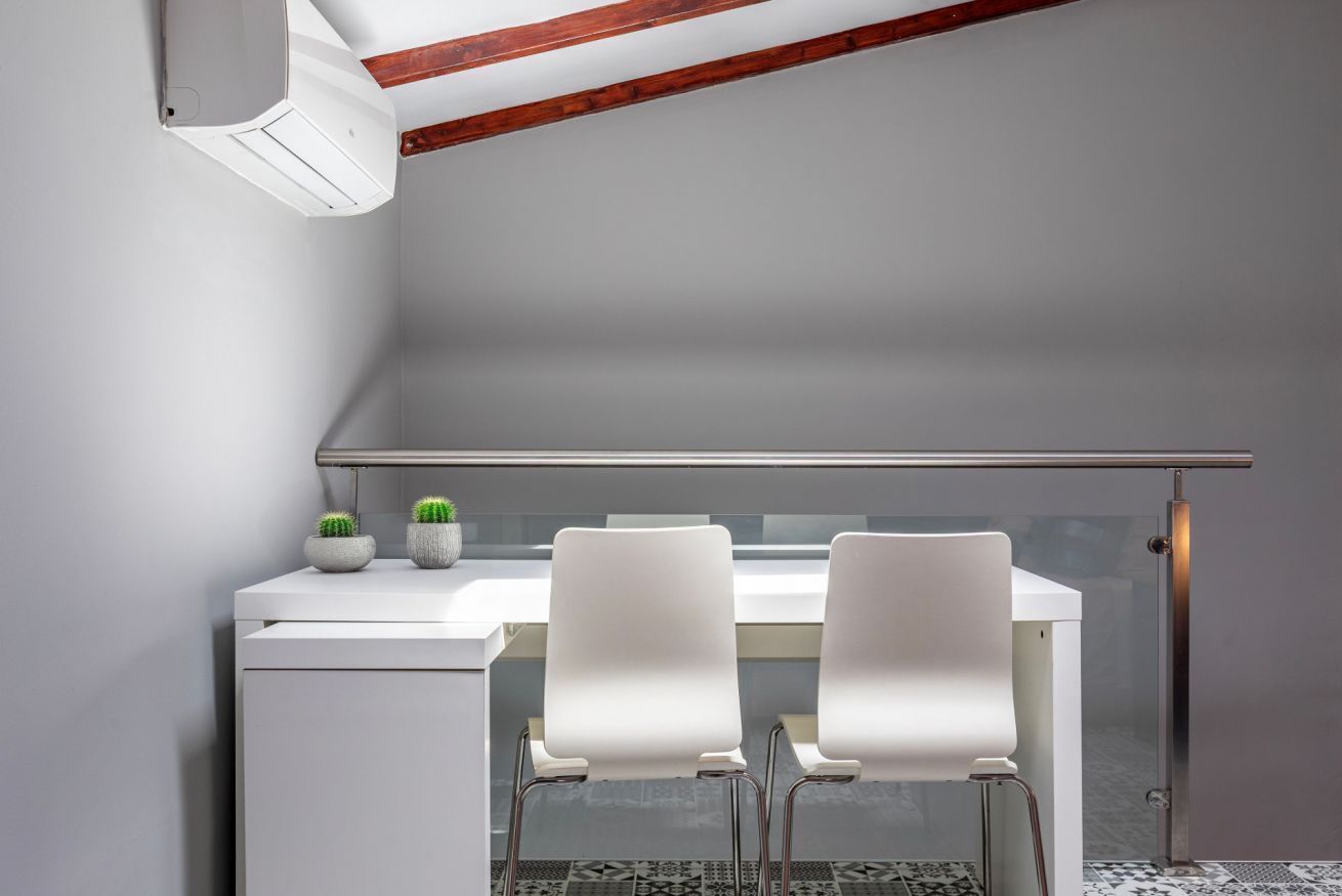 A modern kitchen with a white countertop, two white chairs, and two potted plants.