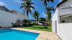 Une piscine dotée d’une terrasse carrelée, entourée d’un mur blanc et de palmiers.