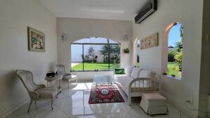 Un salon spacieux avec une grande fenêtre, un canapé blanc, une petite table et un tapis décoratif.