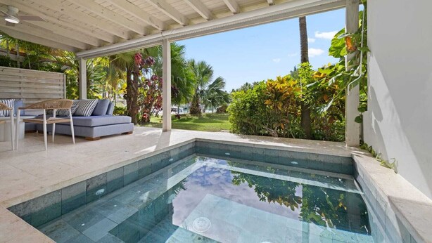 Uma área de piscina moderna com vista ampla para o exterior, um espaço de estar com sofá e cadeiras, e um jardim bem cuidado.