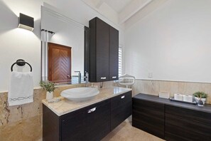 A modern bathroom with a large mirror, a vessel sink, dark cabinetry, and a towel rack.