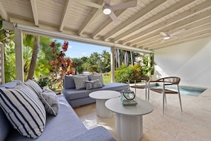A modern outdoor living area with a sofa, two round tables, a chair, and a pool.