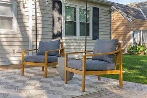 Deux chaises en bois avec des coussins gris, posées sur un tapis d’extérieur à motifs.