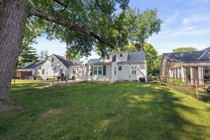 A residential area with multiple houses, a grassy yard, and a large tree providing shade. - Walk to Stadium & Campus -4BR with Game Room (Columbus)