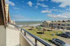 A seaside hotel with a balcony overlooking the ocean, a playground, and multiple cars parked in the driveway.